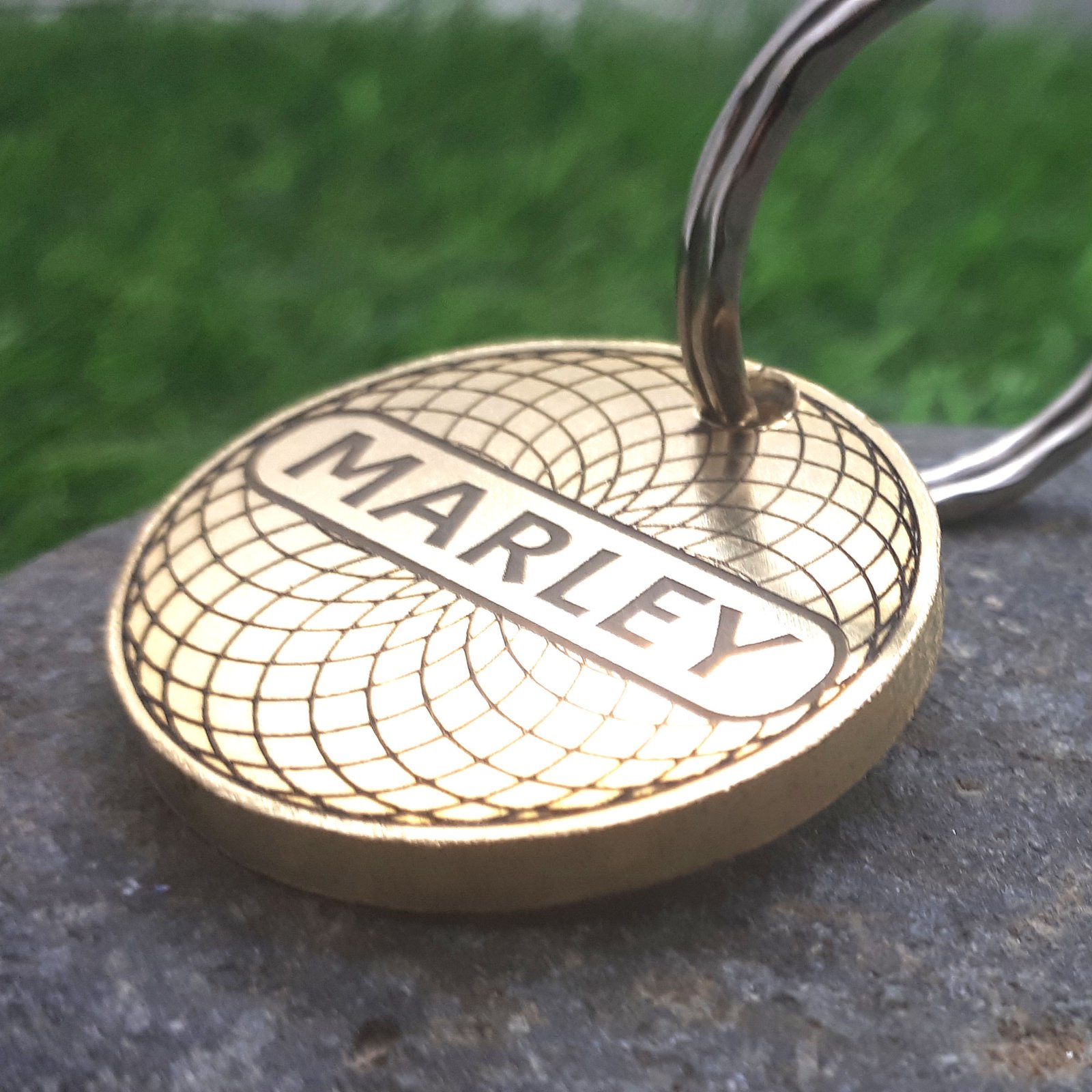 Luxury engine-turned brass pet ID tag with engraved circular pattern and nameplate centre, attached to a stainless steel split ring.